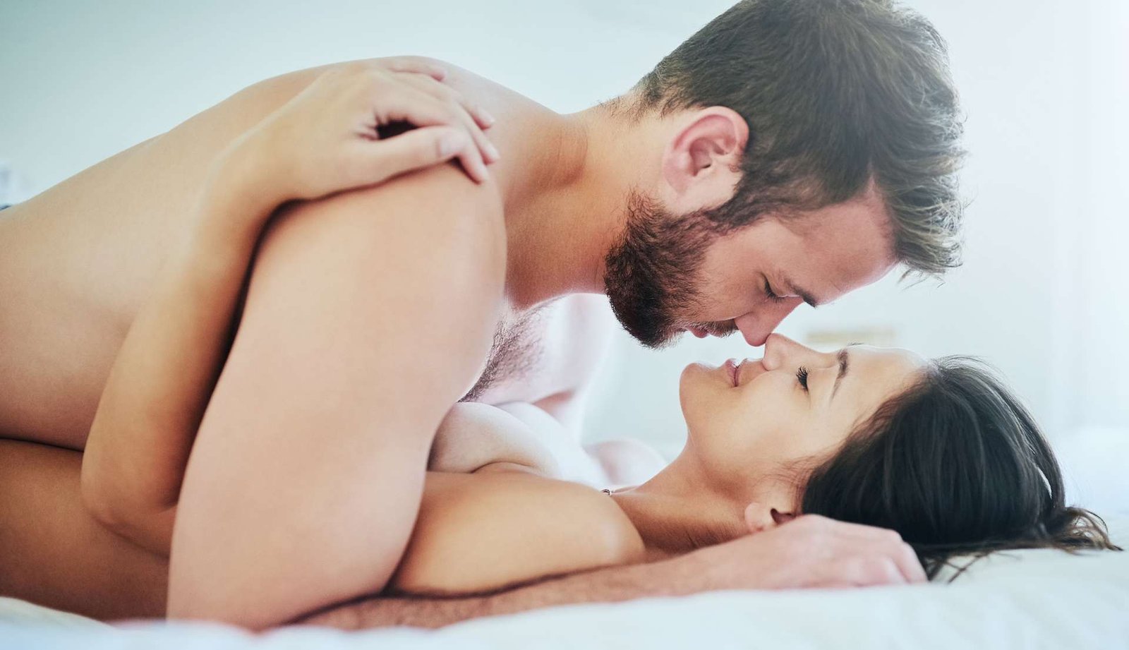 Pareja abrazada en la cama haciendo sexo en la postura del misionero 